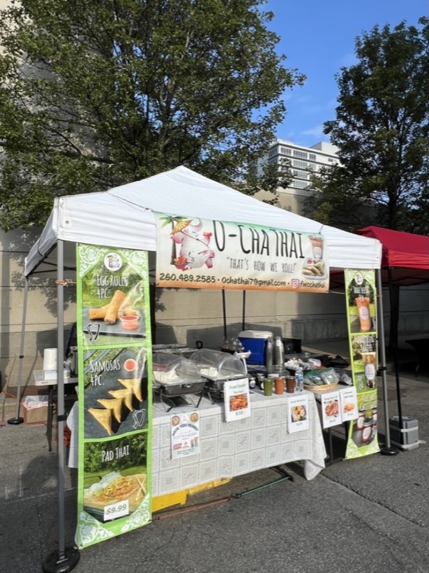 The O-Cha Thai tent at YLNI Farmers Market with banners for egg rolls, samosas and pad thai